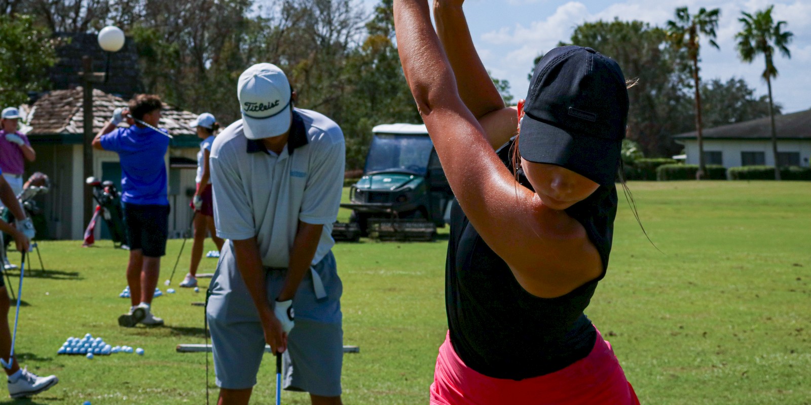 People practicing golf swings on a grassy field, with clubs and training aids visible.